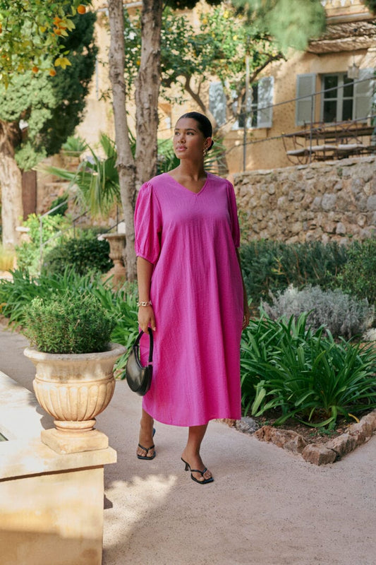 En herlig lang kjole i rosa som er lett og ledig i fasongen og perfekt for sommeren! Kreppstoffet i bomull gjør kjolen luftig. V-hals, korte ermer med strikk og praktiske lommer.  Fra Kaffe Curve.