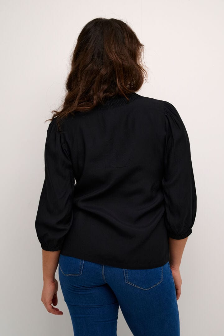 En herlig sort bluse med den populære rysjekanten rundt kragen fra Kaffe! Blusen har v-hals og 3/4 lange ermer med strikk og rynkesøm på skulderne som gjør den ekstra fin.