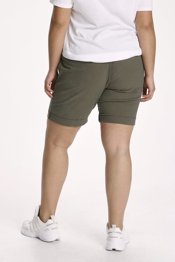 Myk armygrønn shorts med god stretch og strikk i livet med lommer fra Kaffe Curve. Snøre i livet gjør shortsen justerbar. Bena har en liten oppbrett som en fin detalj.