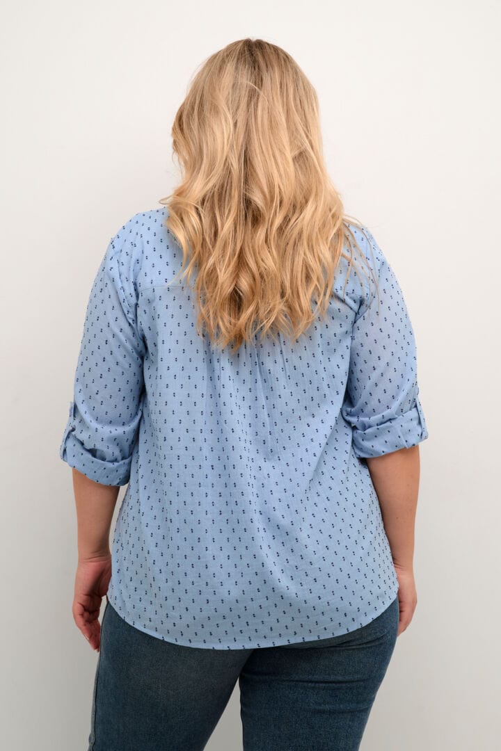 En skjønn langermet skjorte fra Kaffe Curve i lyseblå med mørkeblå prikker. FIn  v-hals, knappestolpe i front og hemper på ermene for oppbrett. Dette er godskjorta og super til olabuksa.