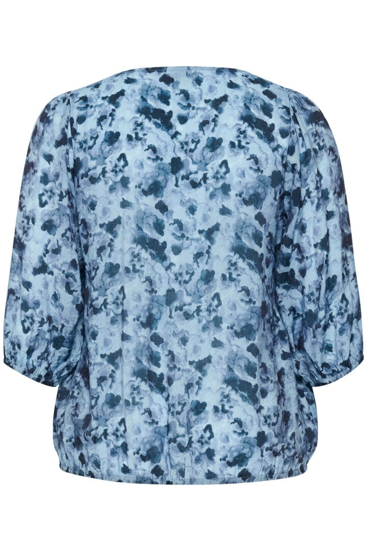 En frisk og herlig bluse med blått mønster og v-hals. Små rynker på skulderne som gir et løft og strikk i ermer og i nederste kant som gir en lekker passform på blusen. Bakside fra Kaffe Curve.