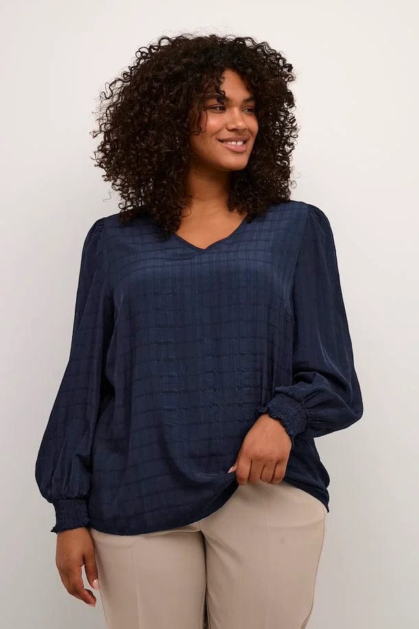 En herlig marineblå bluse med lange ermer og strikk fra Kaffe Curve. Blusen har et vevet mønster, v-hals og små puffer på skulderne som en fin detalj. Kombiner med jeans eller dressbukse.