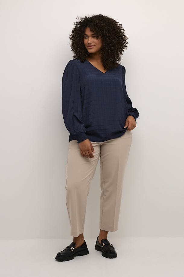 En herlig marineblå bluse med lange ermer og strikk. Blusen fra Kaffe Curve har et vevet mønster, v-hals og små puffer på skulderne som en fin detalj. Kombiner med jeans eller dressbukse.